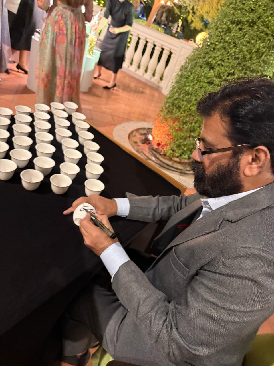 Alfirdous, Pakistani calligrapher in Dubai, engaging with guests through custom Arabic calligraphy at Kempinski Hotel Jumeirah’s luxury calligraphy event.